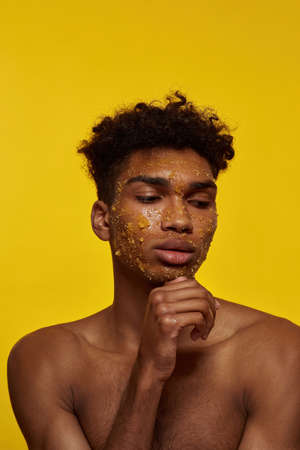 Thoughtful black guy with honey scrub on face skinの写真素材