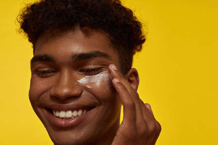 Guy smearing cosmetic cream on his clean faceの写真素材
