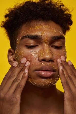 Serious african guy touching face with honey scrubの写真素材