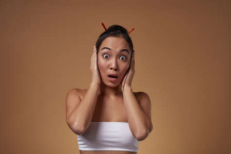 Shocked asian girl with open mouth covering earsの写真素材