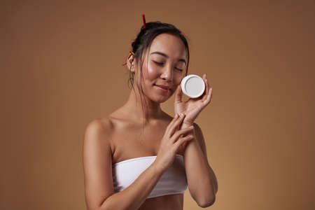 Asian girl with closed eyes holding cosmetic creamの写真素材