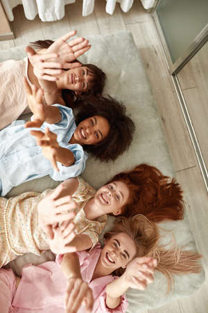 Multiethnic girlfriends pulling hands up on bedの写真素材