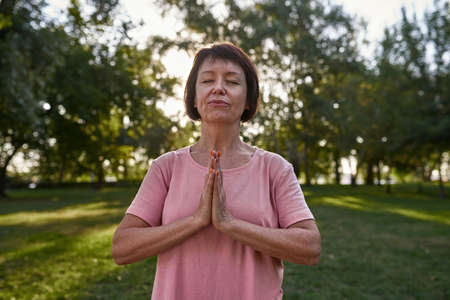 Focused senior woman with closed eyes meditating