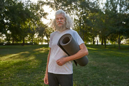 Grey hair man with fitness mat on meadow in parkの写真素材