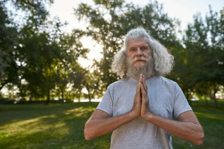Elderly man practicing yoga and meditating in parkの写真素材