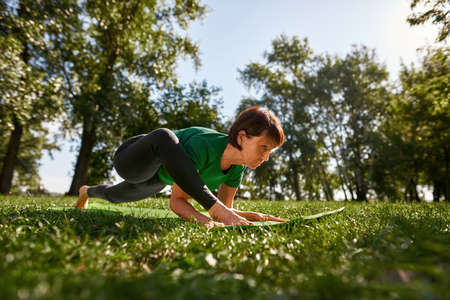 Focused senior woman practicing yoga in sunny parkの写真素材