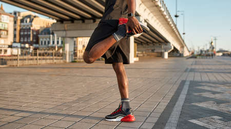 Cropped of black sportsman warming up leg in city