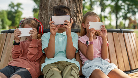 Obscure faces of children use smartphones on bench