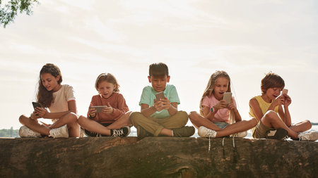 Emotional kids watch smartphones on river coastの写真素材