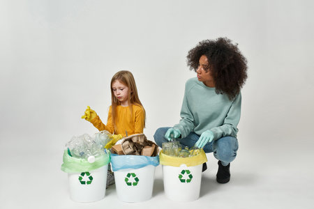 Multiracial girls wear gloves sort garbage in binsの写真素材