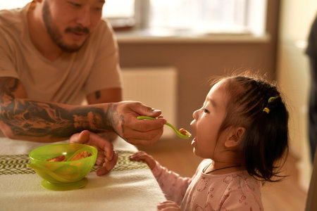 Father feeding little daughter cheese curd fritterの写真素材