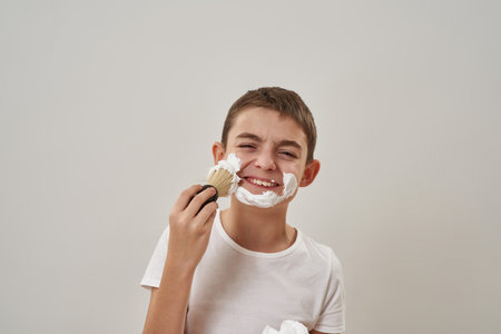 Cropped boy smear shaving foam on face with brush