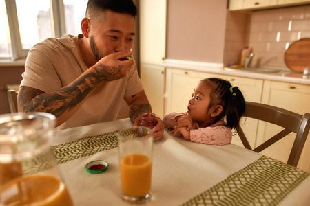 Asian little girl looking at father eat baby foodの写真素材