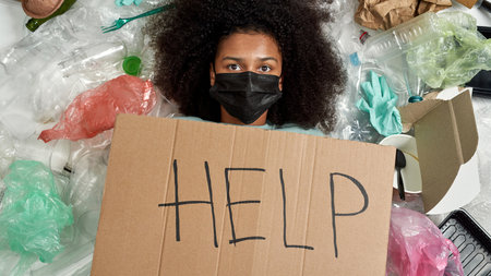 Black girl with Help placard lying in garbage