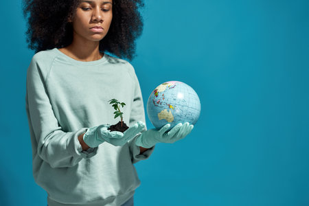 Girl hold and look at globe and plant in ground