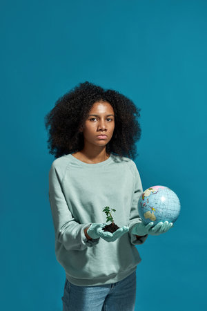 Black girl holding globe and green plant in ground