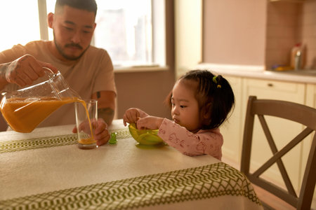 Father pour juice in cup while her daughter eatの写真素材