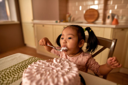 Girl eating big sweet cake with spoon at tableの写真素材