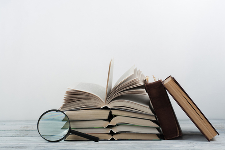 Open book, hardback colorful books on wooden table. Magnifier. Back to school. Copy space for text. Education business concept.の写真素材