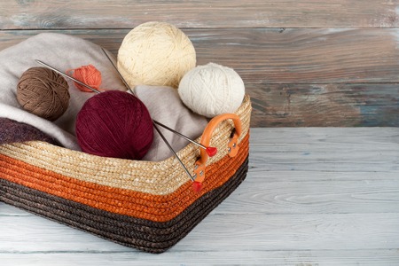 Ball of wool, needles and woolen sweater with spokes for handmade knitting in basket on wooden table