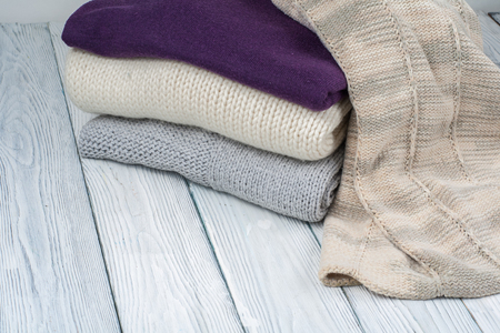 Knitted wool sweaters. Pile of knitted winter clothes on wooden background, sweaters, knitwear,...