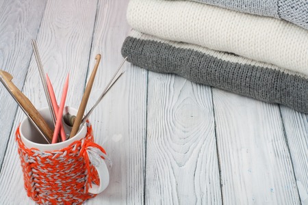 Knitted wool sweaters. Pile of knitted winter, autumn clothes on wooden background, sweaters,...