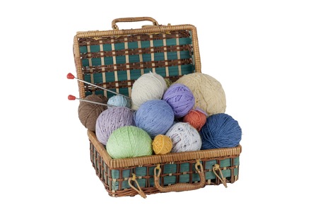 Ball of wool, needles and woolen sweater with spokes for handmade knitting in basket on wooden table.の写真素材