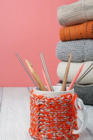 Knitted wool sweaters. Pile of knitted winter, autumn clothes on wooden background, sweaters, knitwear, cup, pen, leaf space for text.の写真素材