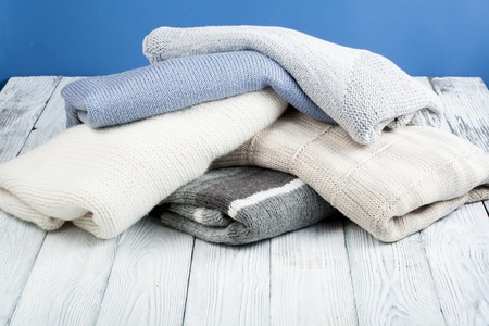 Knitted wool sweaters. Pile of knitted winter, autumn clothes on blue, wooden background, sweaters, knitwear, space for textの写真素材