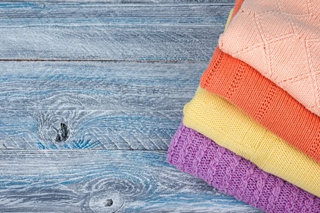 Knitted wool sweaters. Pile of knitted summer clothes on wooden background, sweaters, knitwear, space for text.の写真素材