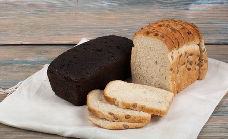 Many mixed breads and rolls of baked bread on wooden table background.