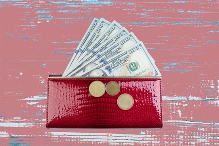 red leather wallet with dollar bill on wood table.