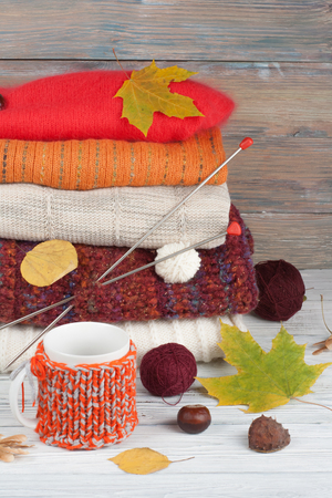 Knitted wool sweaters. Pile of knitted winter, autumn clothes on red, wooden background, sweaters, knitwear, ball, cup, leaf space for text.の写真素材