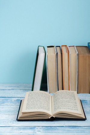 Book stacking. Open book, hardback books on wooden table and blue background. Back to school. Copy space for textの写真素材