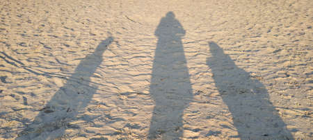 Three human shadows on a yellow brown surface, two adults and one child.の写真素材