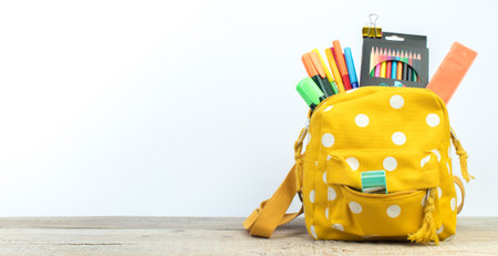 Yellow backpack with white polka dots with different colorful stationery on table. white background. back to school. banner designの写真素材