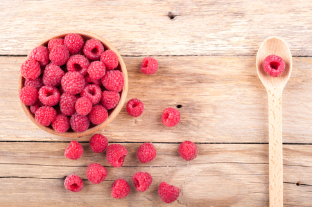 Fresh ripe raspberries in a bowl and spoon with berry on old wooden table. Copy space, top view