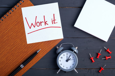 Sticky note with word Work it. White note paper, planner, pen and clock on a wooden background. Office workplace. Copyspace. Top viewの写真素材