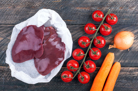Raw liver and vegetables tomatoes, carrots and onion on rustic wooden background. Ingredients for liver or pate. Top viewの写真素材