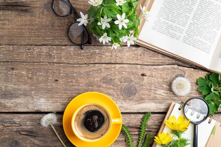 Open book, cup of coffee, bouquet of flowers, pen, notebook, glasses and magnifier on old wooden background. Office desk table. Work, studying, educations, reading, botanical concept. Top view, copy spaceの写真素材