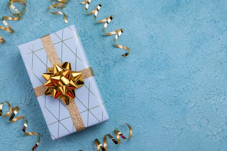 Holidays gift box wrapped in blue geometric paper on blue background. Happy Holidays, Christmas,...