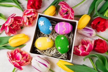 Easter background with colorful knitted Easter eggs and tulip flowers on stone background.  Easter...