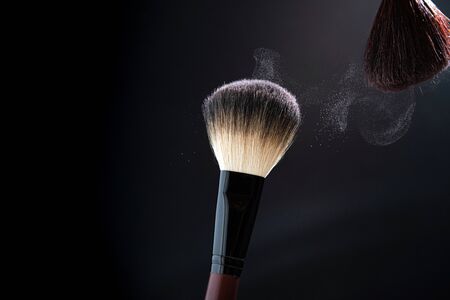 Makeup brush with powder explosion on black background. Cosmetics, beauty accessories, make up,...