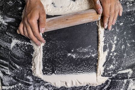 Female hands with rolling pin with flour on dark table. Baking background. Flour, cooking and baking...