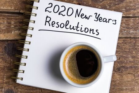 New year resolutions 2020 on desk. 2020 goals list with notebook, coffee cup on wooden background. Goals, plan, strategy, change, action, idea conceptの写真素材