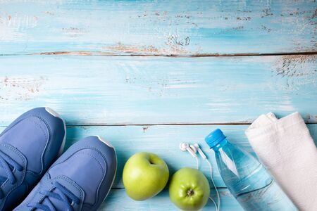 Flat lay sport shoes, bottle of water, apples, towel and earphones on blue wooden background. Healthy lifestyle, sport and diet concept. Top view, copy spaceの写真素材
