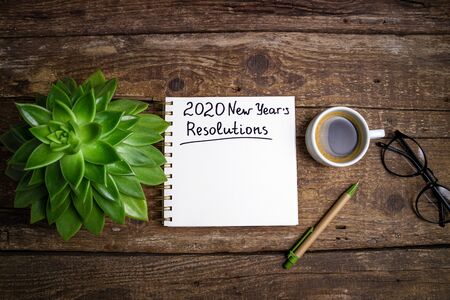 New year resolutions 2020 on desk. 2020 goals list with notebook, coffee cup and eyeglasses on...