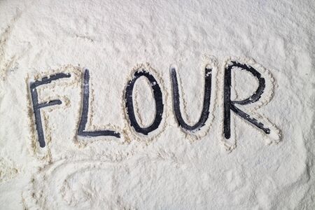 White flour on dark table. Baking background. Flour texture with word flour. Top viewの写真素材