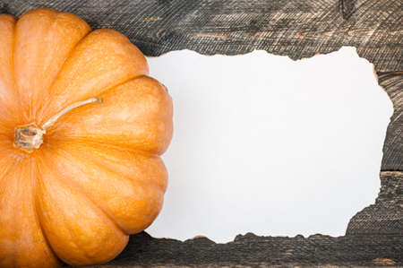 Pumpkin on old dark rustic wooden table. Halloween background with pumpkin and white blank of old paper. Autumn, halloween concept. Copy space, top viewの写真素材
