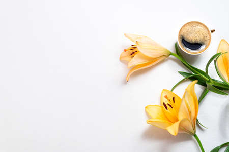 Flowers lily and coffee cup on white background. Coffee break, floral card, cozy home breakfast concept, top view, flat lay. Copy spaceの写真素材